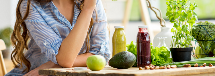 Blog of Natural Ways to Cleanse and Restore Your Gut which have image A woman in a blue striped shirt sits at a wooden table surrounded by fresh fruits, vegetables, green herbs, and two colorful juice bottles.